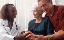 Man and woman sitting next to doctor.  Woman has medicine bottle in her hand.