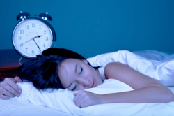 Woman sleeping restfully in bed with alarm clock on night stand next to bed